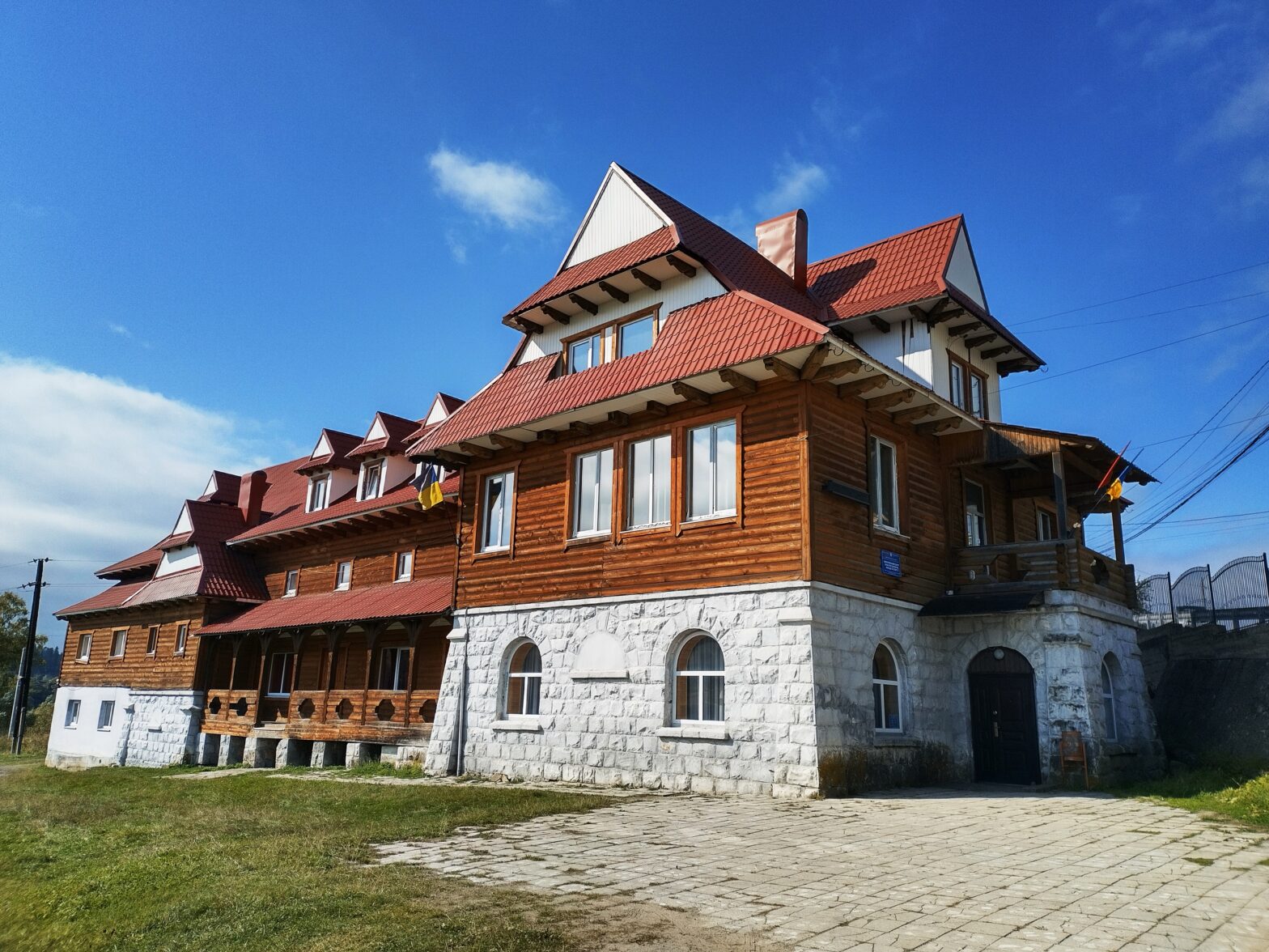 Трьохповерхова дерев'яна будівля із зеленою галявиною навколо та небесною блакиттю на фоні