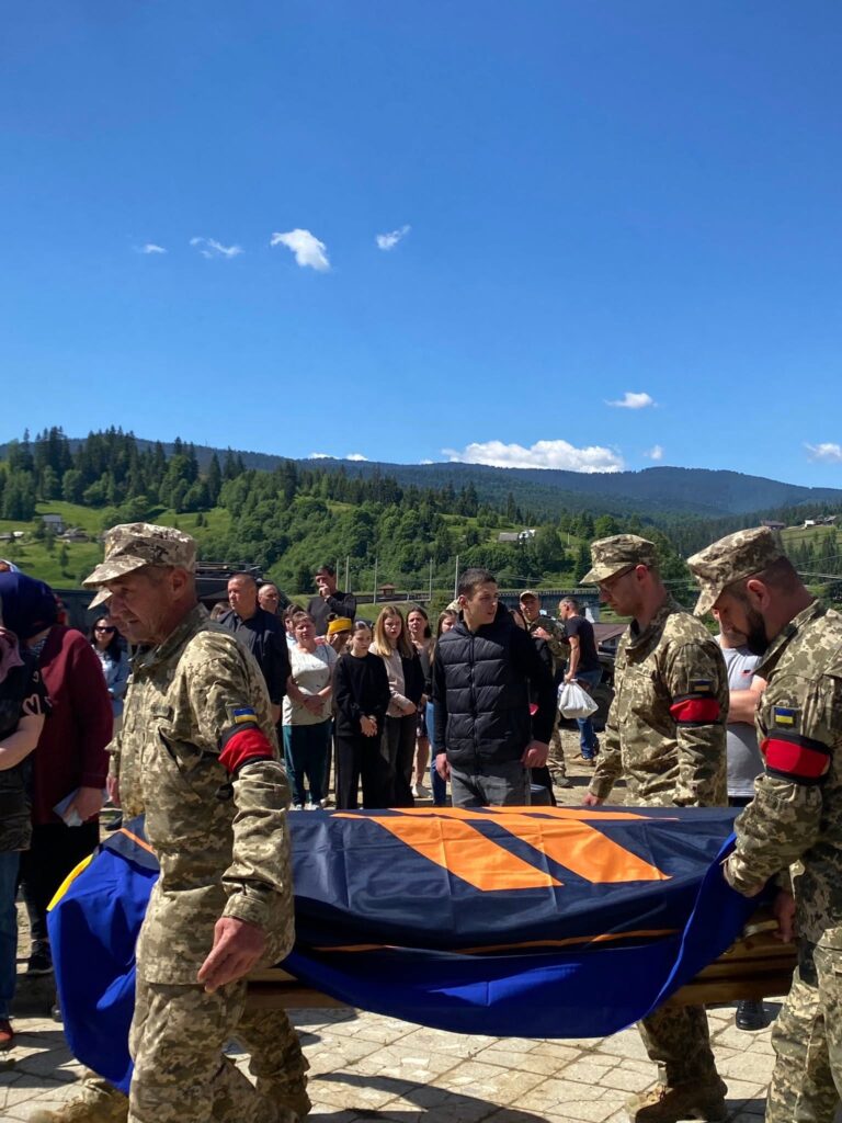 Люди у військовій формі надворі несуть труну