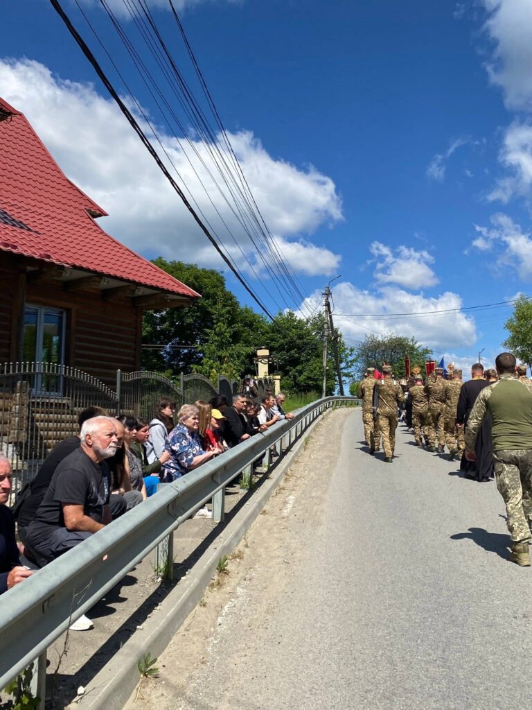 Асфальтована дорога, по якій прямує процесія з руною, а обабіч дороги на колінах стоять люди