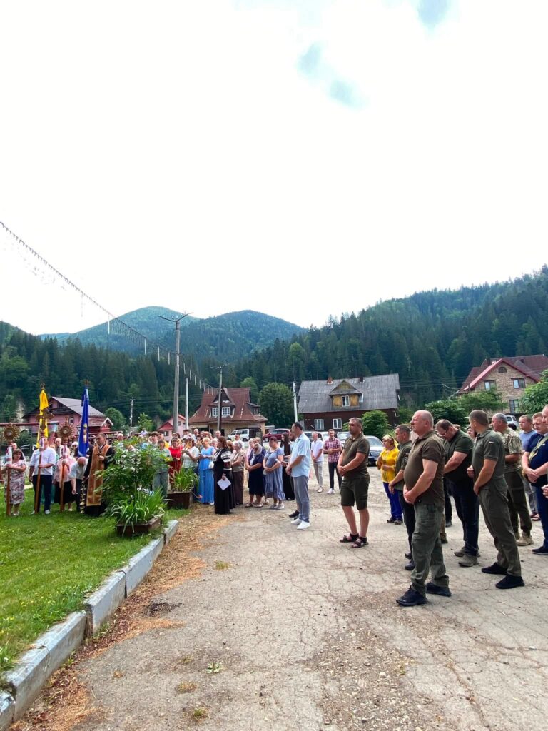 Близько десятка людей стоять на площі, на фоні видніються гори