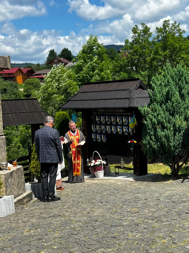 Чоловік у церковній рясі навпроти стенду та ще один чоловік у костюмі