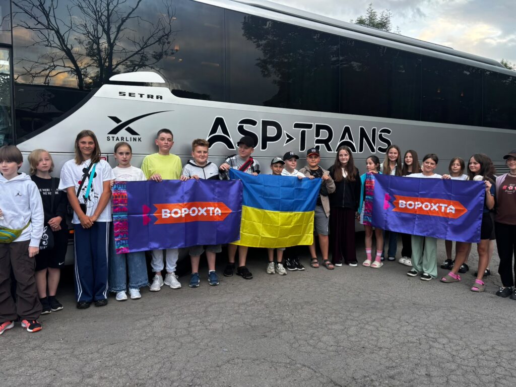 Ближній кадр дітей, що тримають прапор України та Ворохти. Позаду них - автобус
