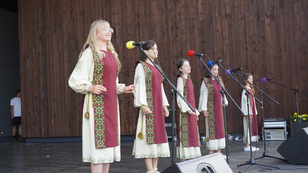 Колектив юних дівчат стоїть перед мікрофонами на сцені у сукнях вишивкою