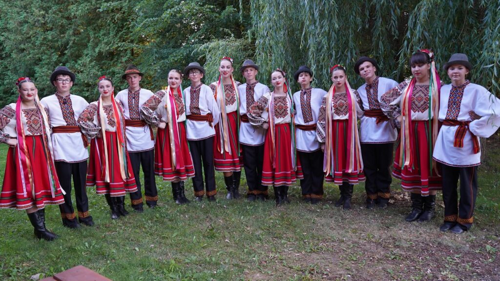 Юнаки з дівчатами позують на камеру з посмішками у вишиванках та яскравих сукнях і капелюхах